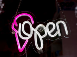Logo lumineux, Open en ayant blanc, avec une glace rose, devant l'entrée de Candy World