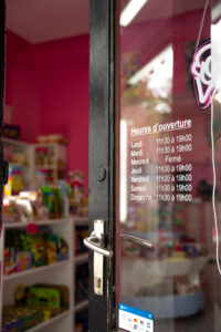 Porte du magasin Candy Word, légèrement ouverte, avec les horaires affichés et un aperçu flou de l'intérieur de la boutique à Bruxelles